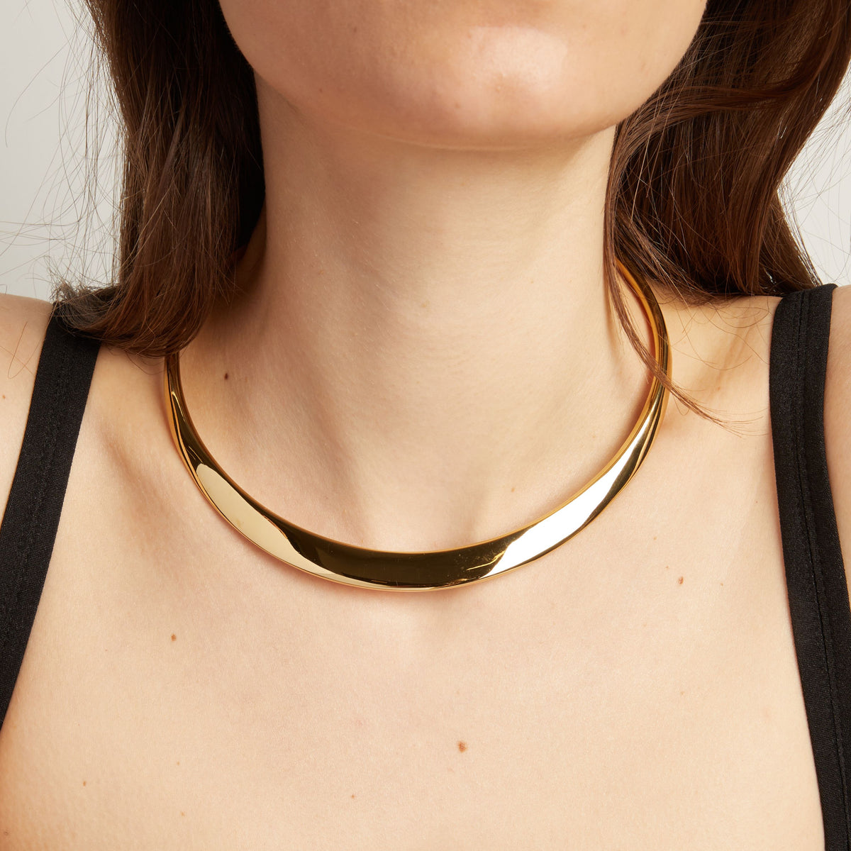 Close up of thick cold collar necklace on woman with neutral background.