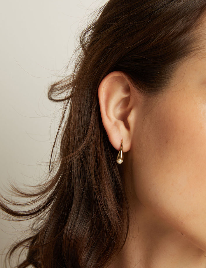 Close-up of a person wearing a gold earring with a neutral background