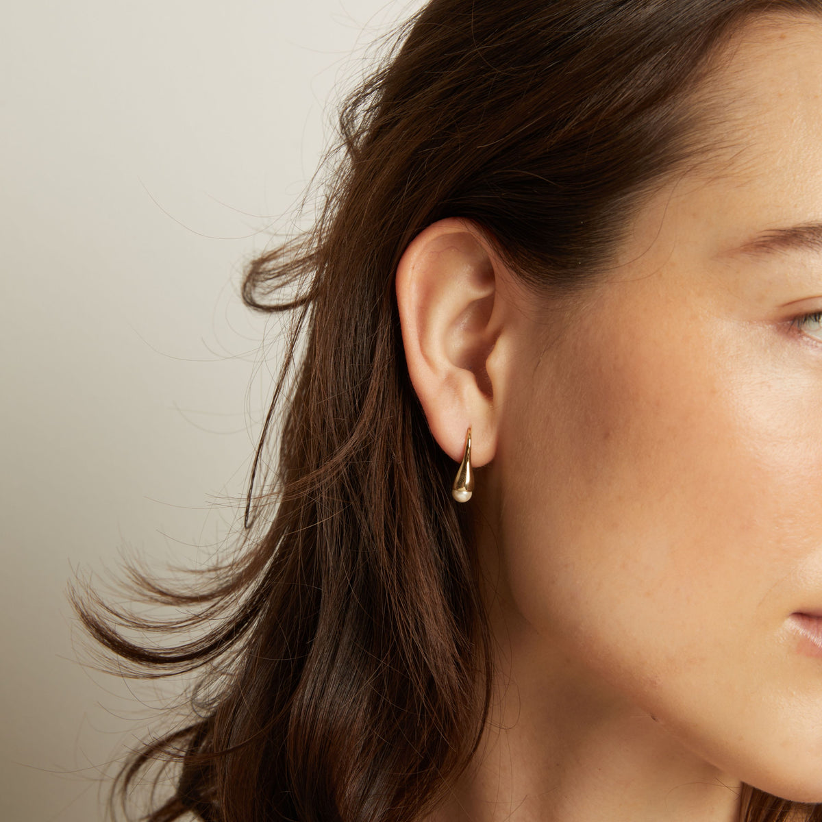 Close-up of a person wearing a gold earring with a neutral background