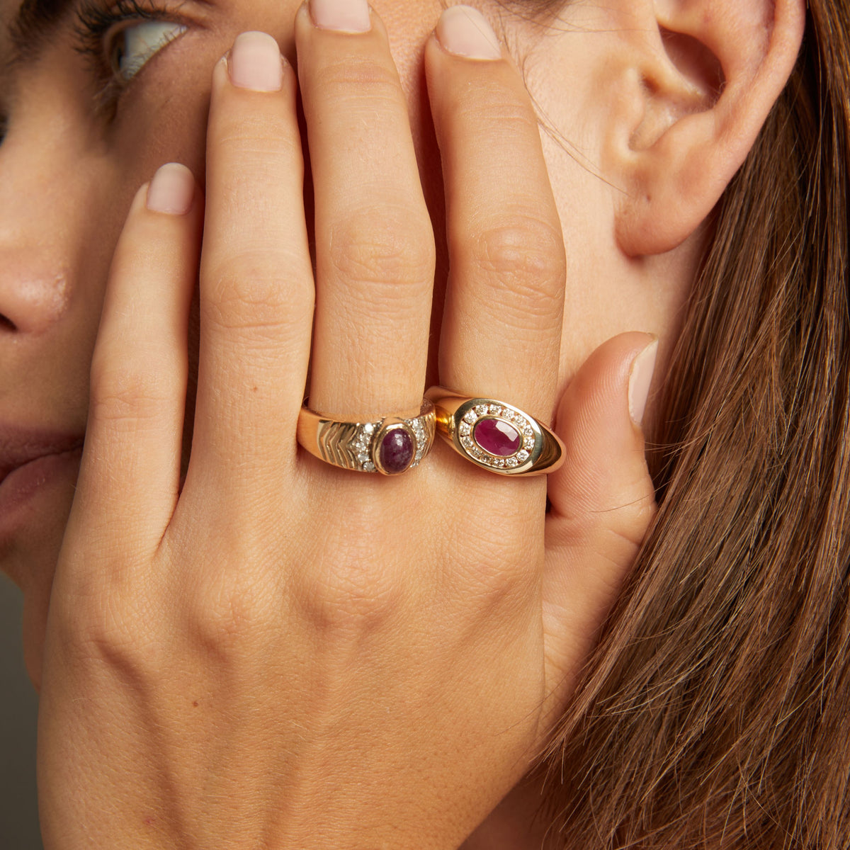 Model. Close up of woman wearing red ruby statement rings on neutral background. 