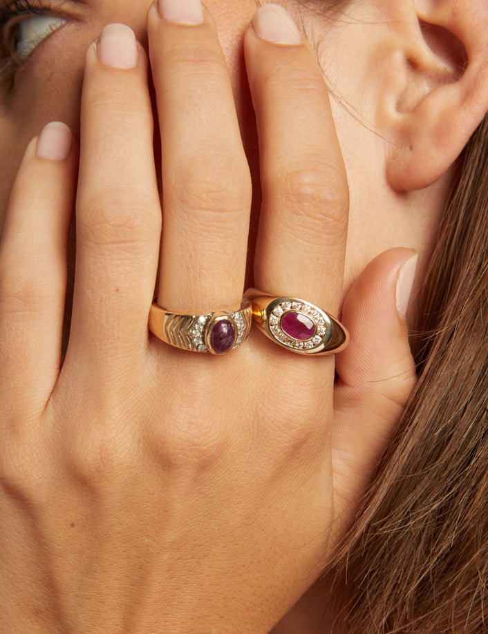 Close up of woman wearing red ruby statement rings on neutral background. 