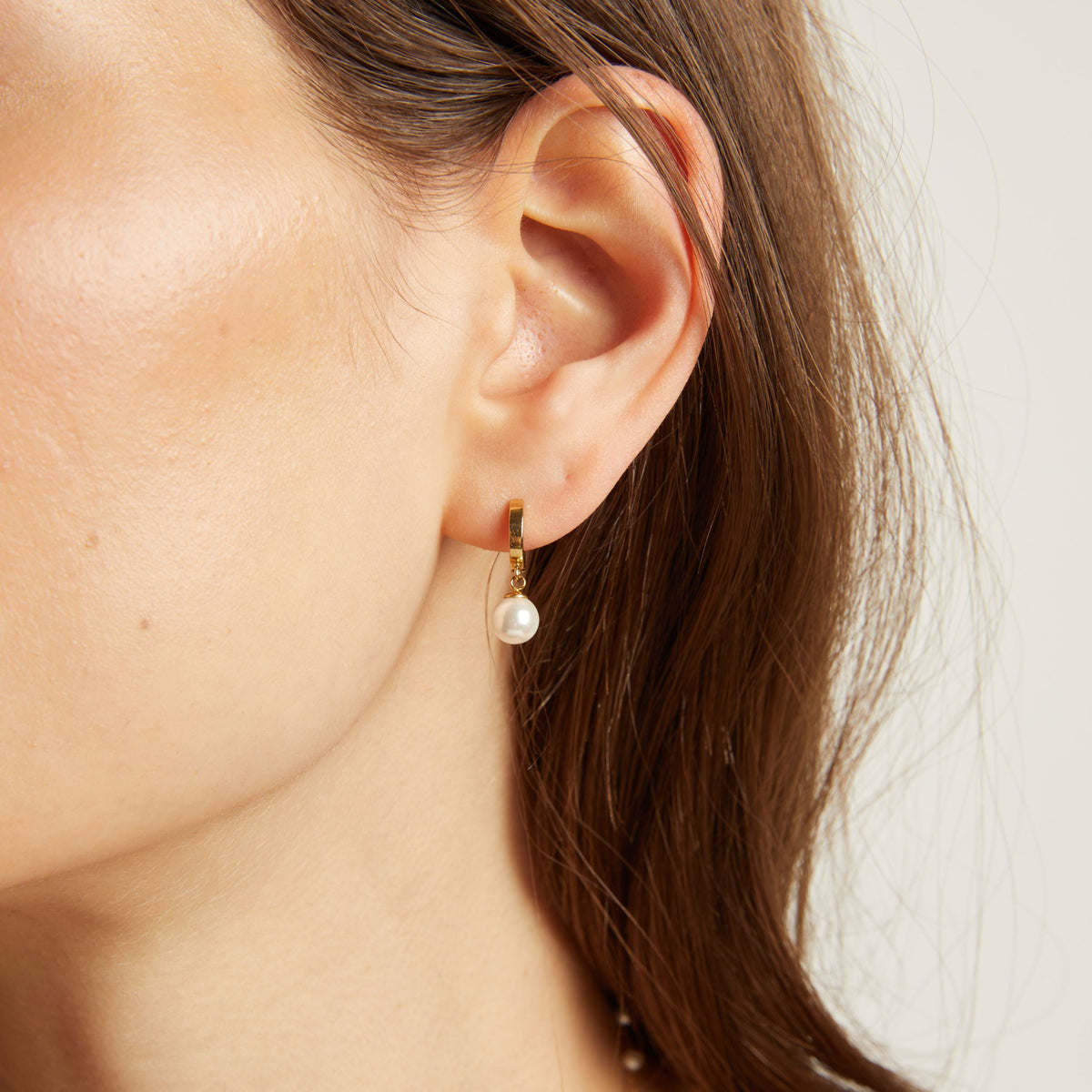 Close up of a person wearing pearl earrings with a neutral background.