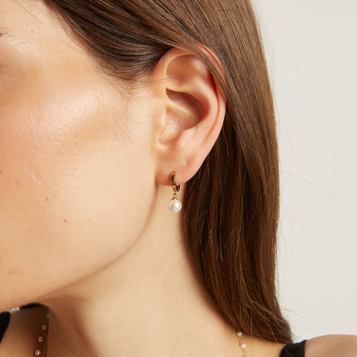 Model. Close up of a person wearing pearl earrings with a neutral background.