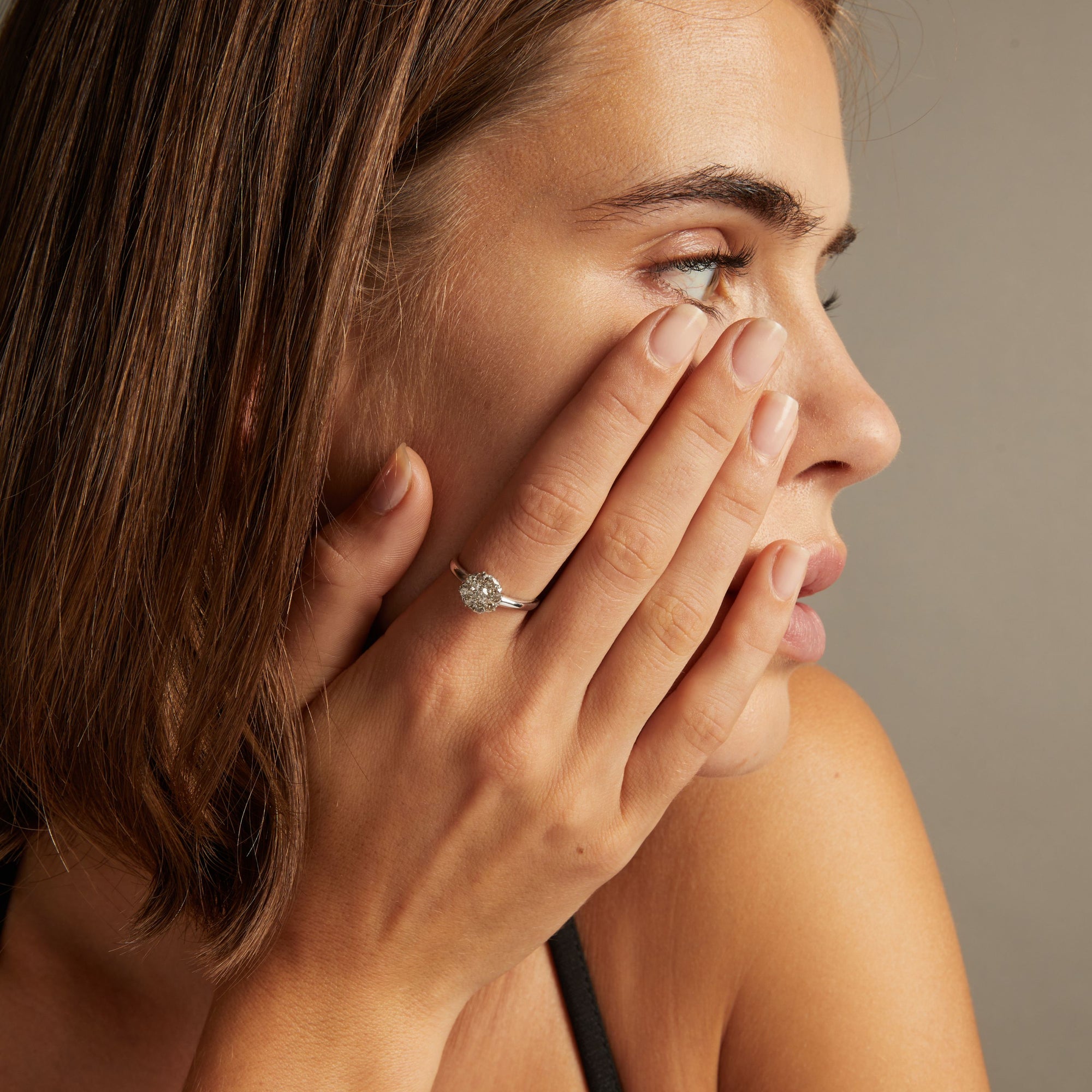 Model. Close up of a woman wearing a diamond flower ring on neutral background.