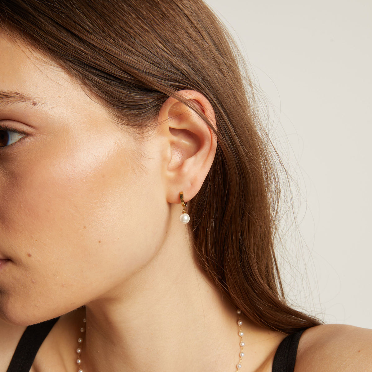 Close up of a person wearing pearl earrings with a neutral background.