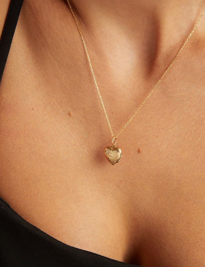 Close up of a woman wearing a gold heart locket on neutral background.