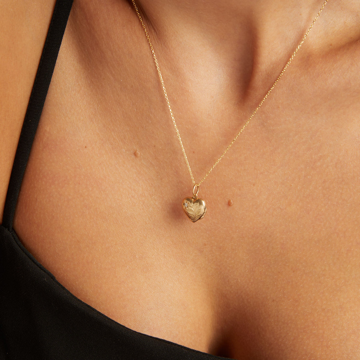 Close up of a woman wearing a gold heart locket on neutral background.