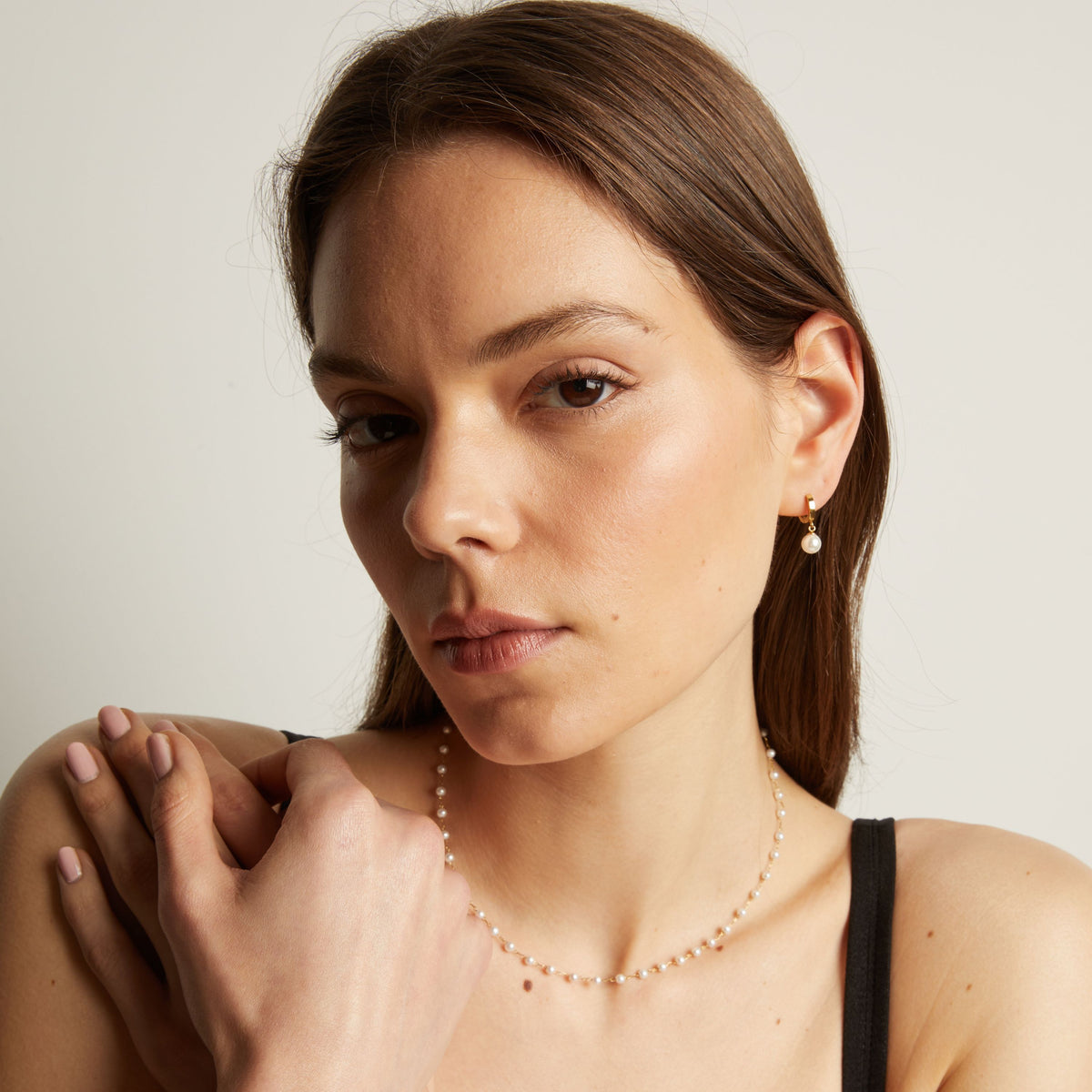 Woman with pearl earring and necklace against a plain background.