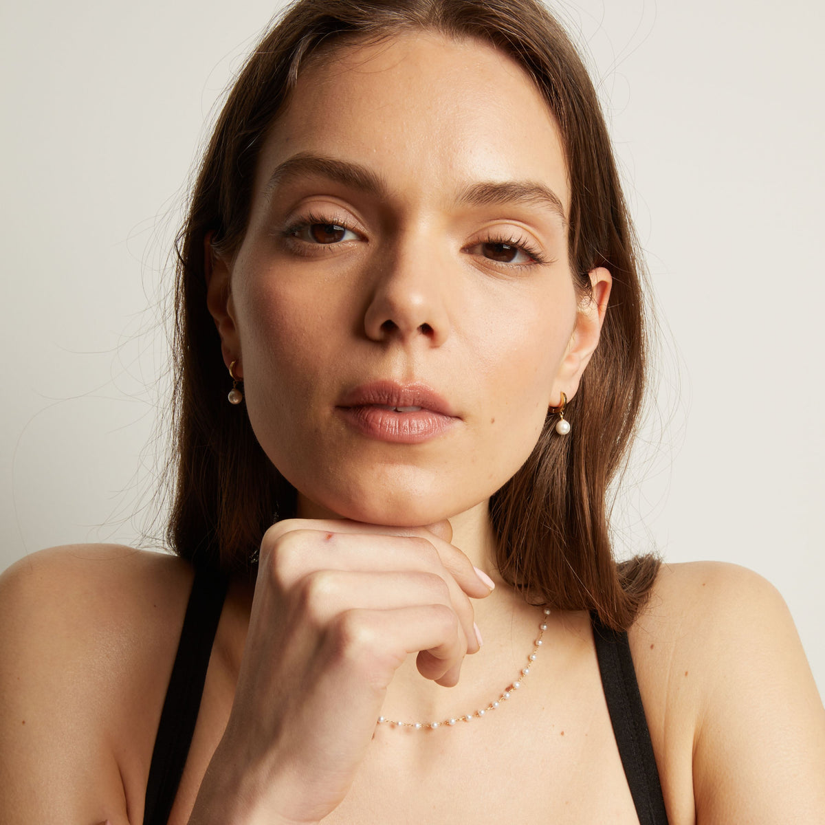 Woman with pearl earring and necklace against a plain background.