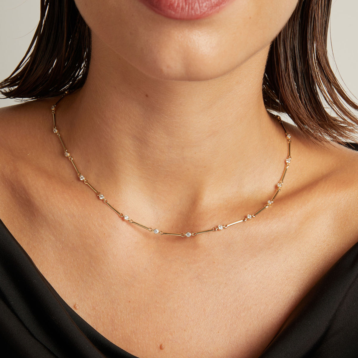 Model. Close up of a woman in a black top wearing a diamond bar necklace on beige background.