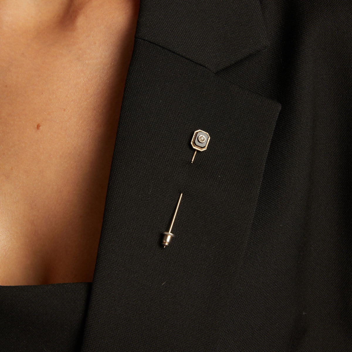 Close up of a woman wearing a black pin on blazer on neutral background.