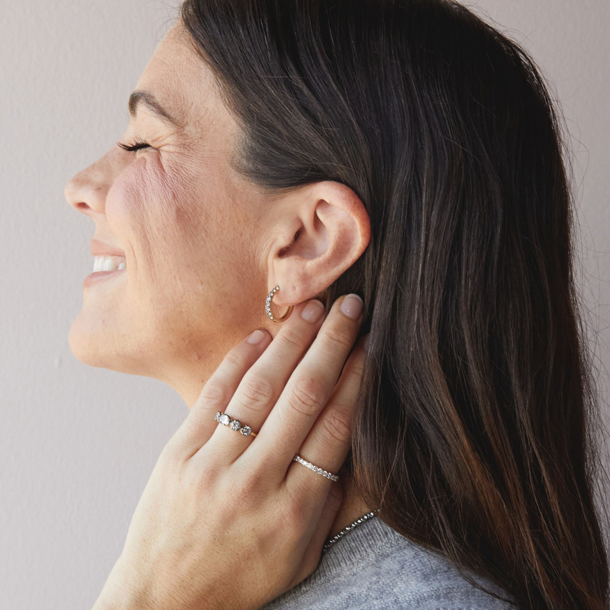 Model. Close up of woman wearing black rhodium huggie earring and gemstone rings. 