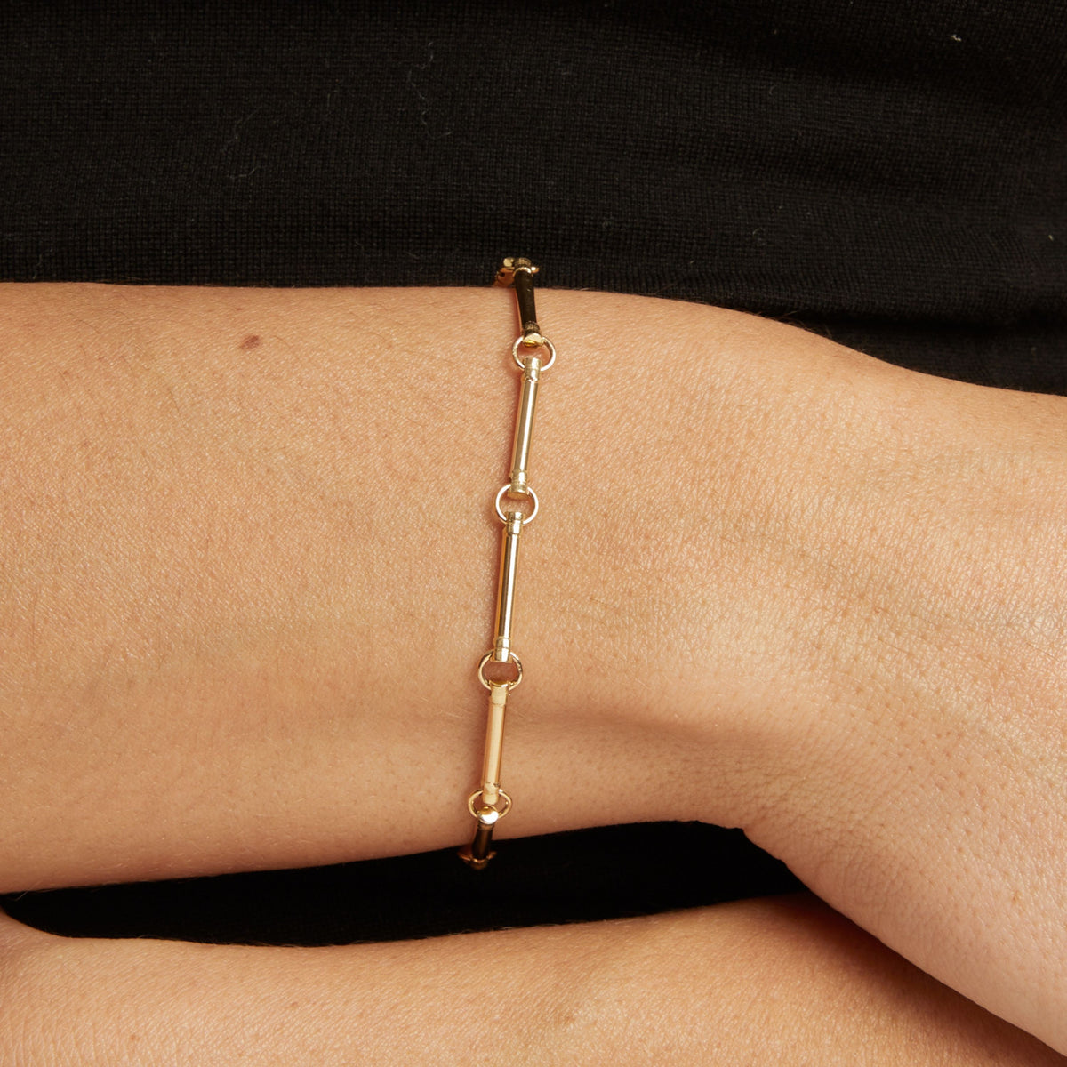 A gold chain bracelet with round links worn on a woman's wrist, shown against a black top.