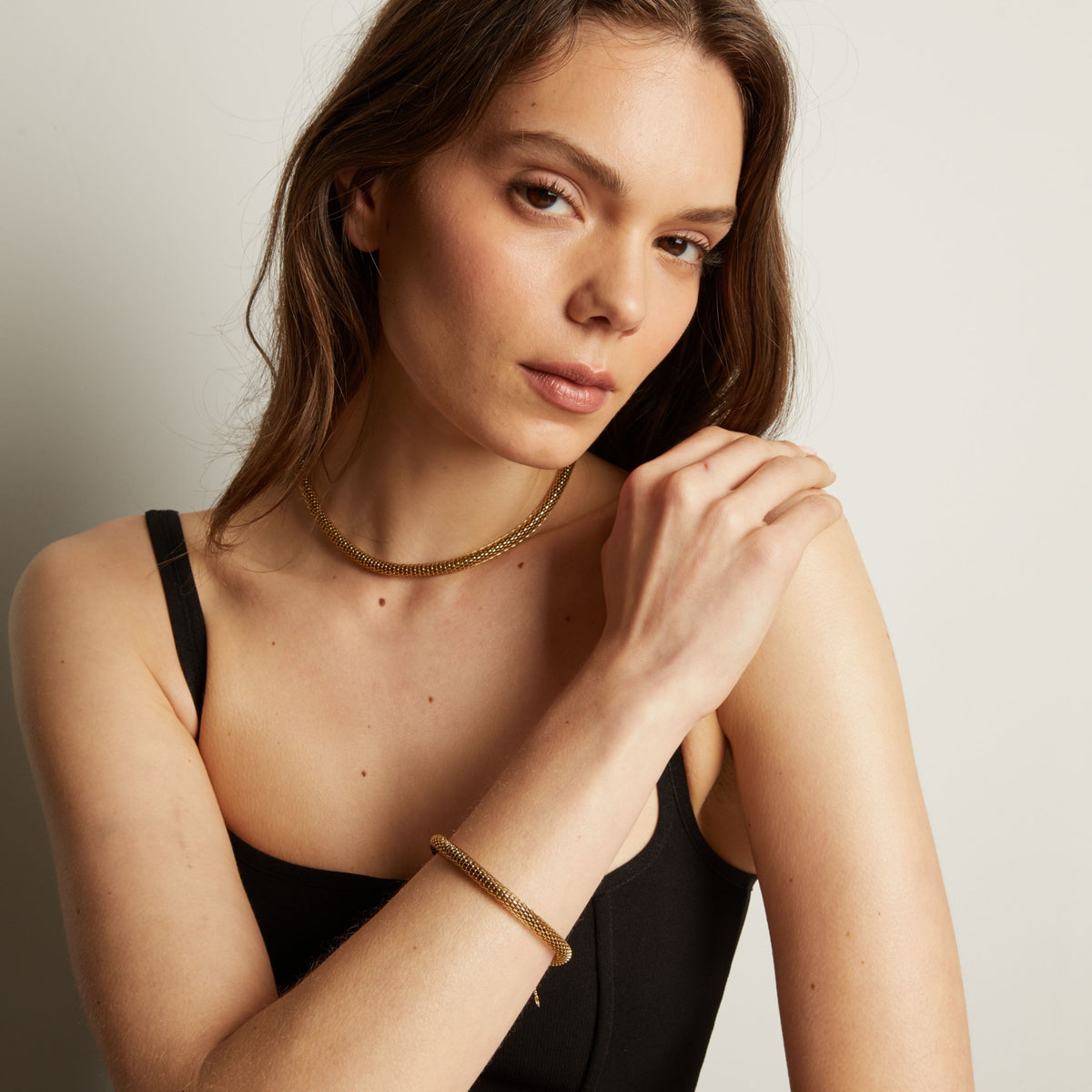 Gold chain bracelet and necklace on woman in black tank top.