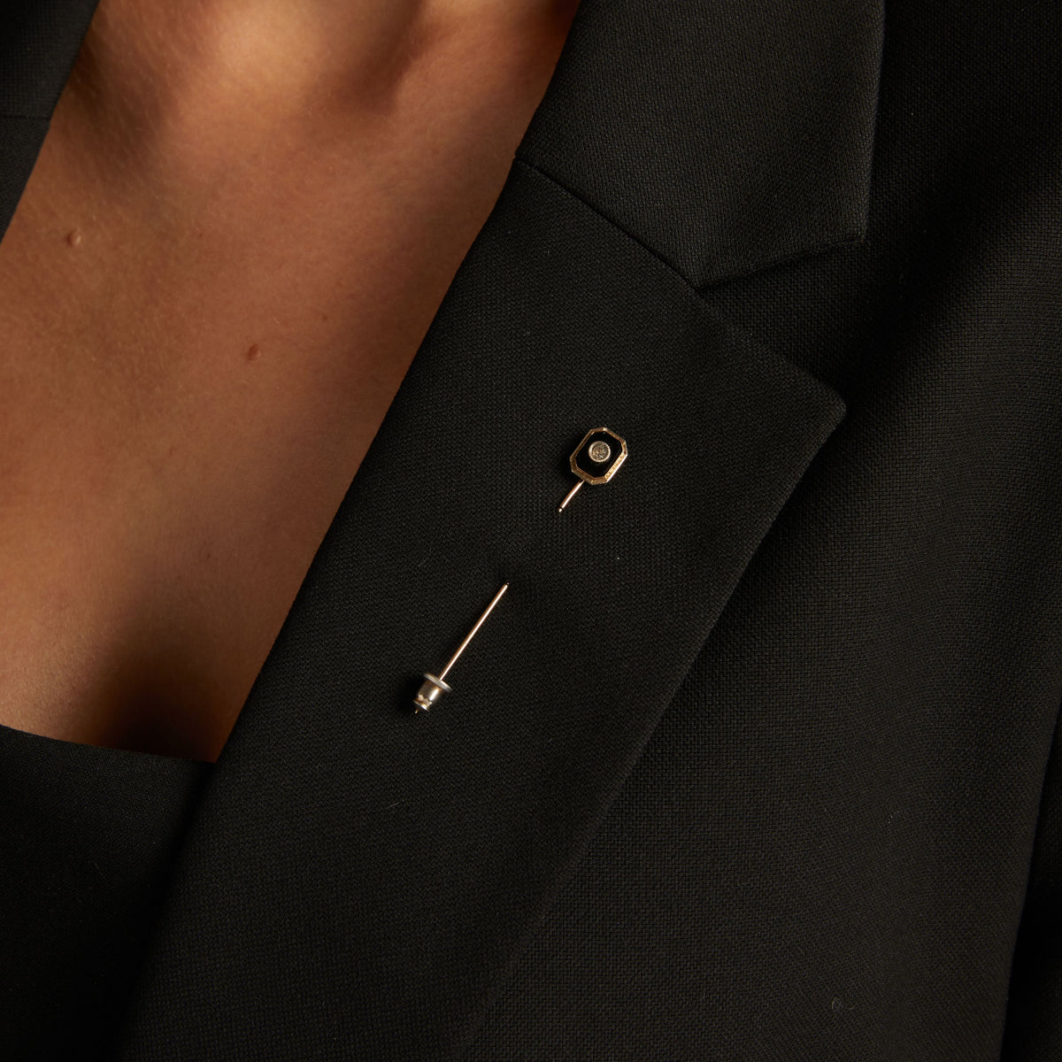 Model. Close up of a woman wearing a black pin on blazer on neutral background.