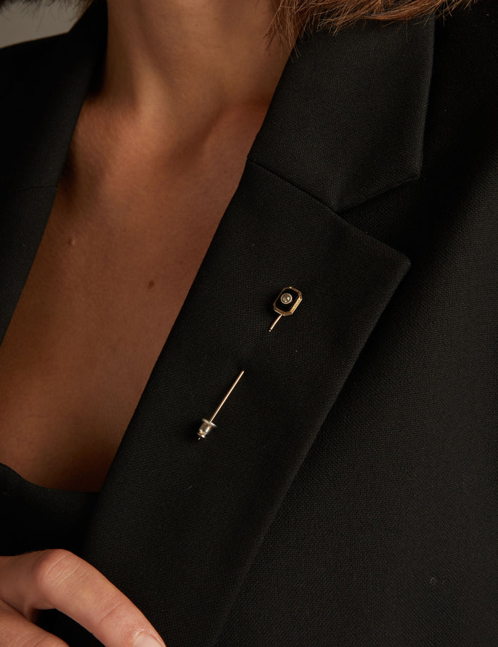 Model. Close up of a woman wearing a black pin on blazer on neutral background.