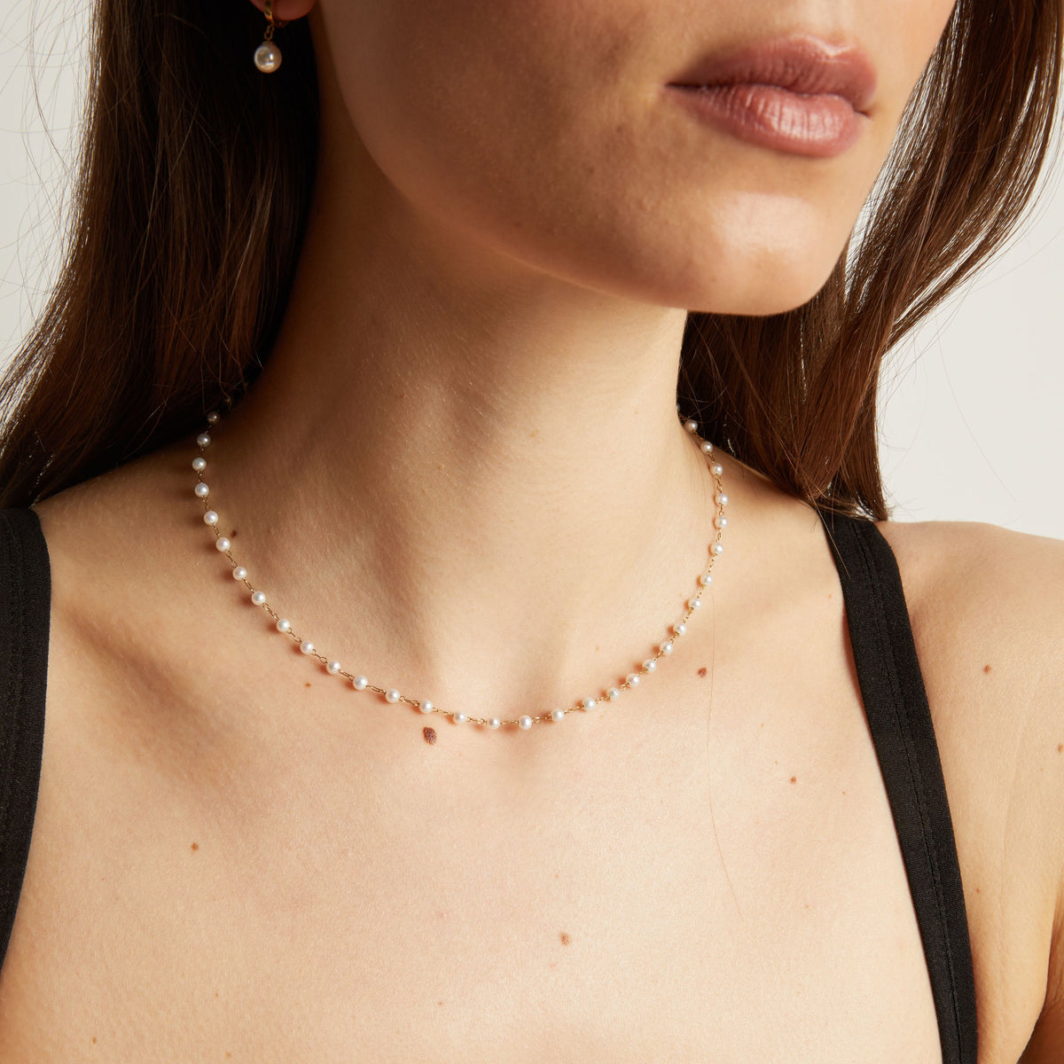 Pearl necklace worn by a person with a neutral background.