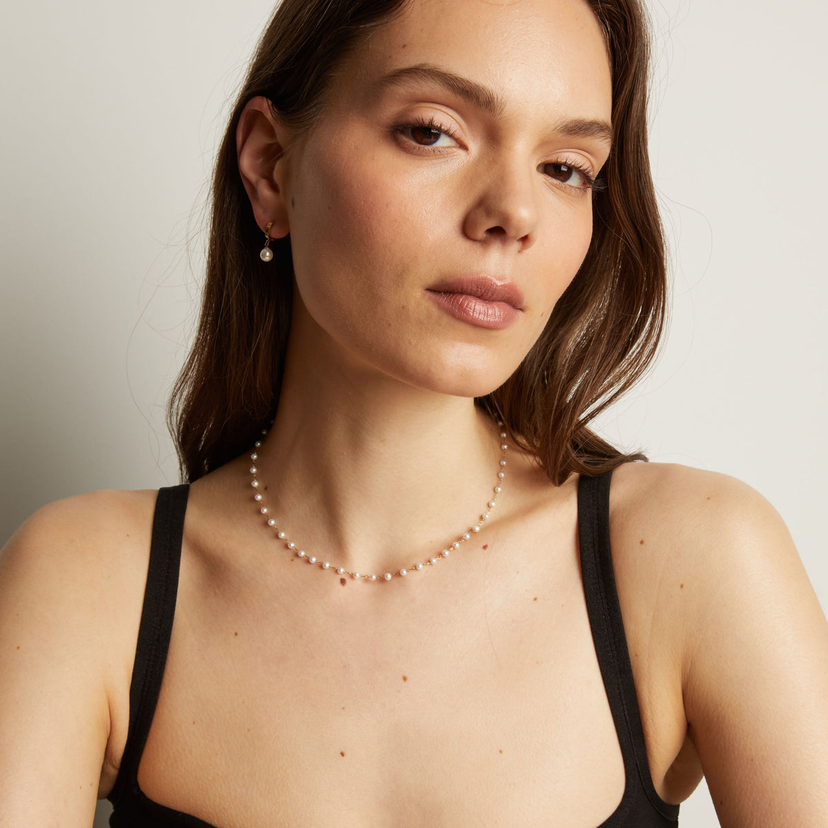 Pearl necklace worn by a person with a neutral background.