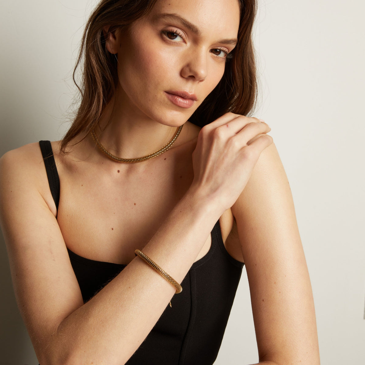 Gold chain bracelet and necklace on woman in black tank top.