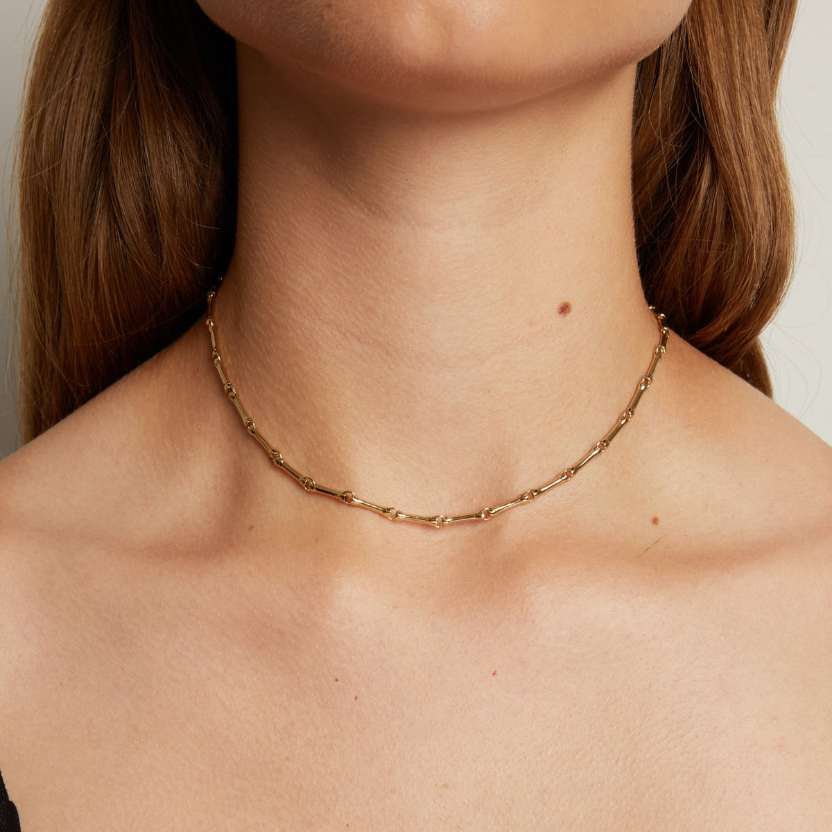 Model. A close-up of a woman's neck wearing a delicate gold chain necklace with a textured, segmented link design.