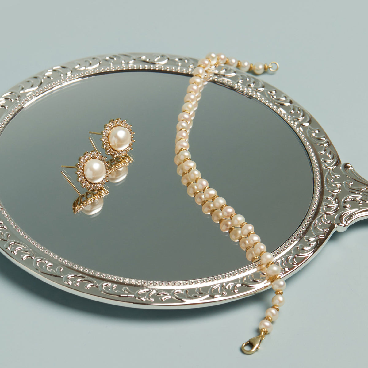 Model. Pearl necklace and earrings on an ornate silver tray with a light blue background