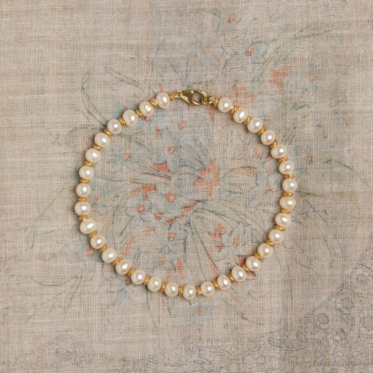 Pearl bracelet with gold accents on a textured fabric background