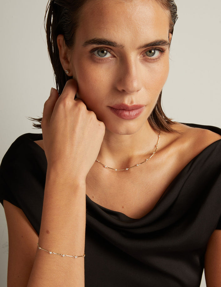 Model. Close up of a woman in a black top wearing a diamond bar necklace and matching bracelet on beige background.
