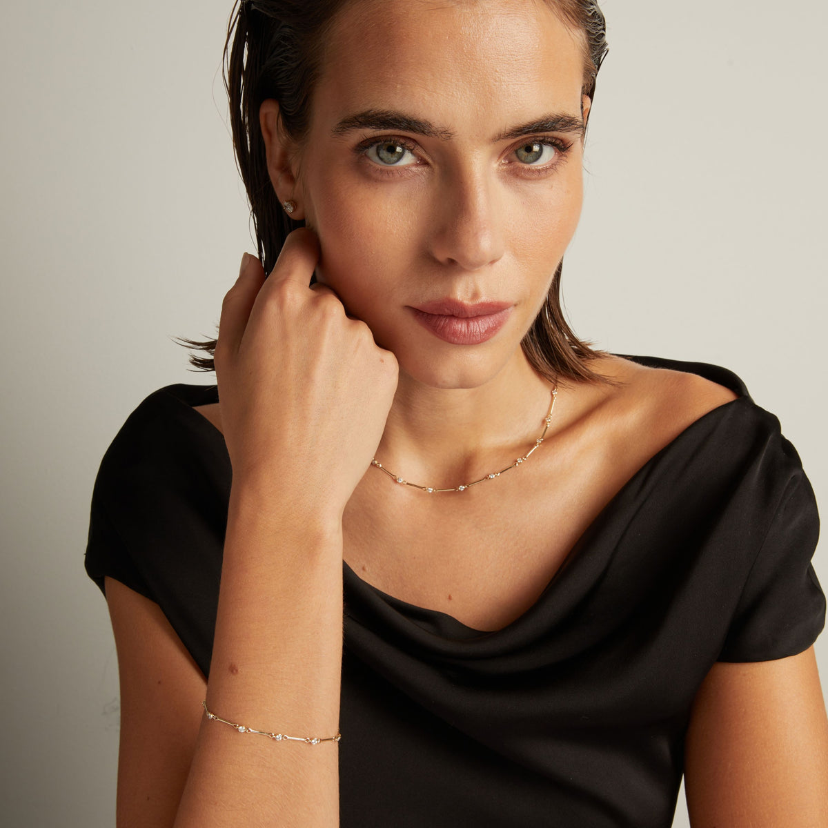 Model. Close up of a woman in a black top wearing a diamond bar necklace and matching bracelet on beige background.
