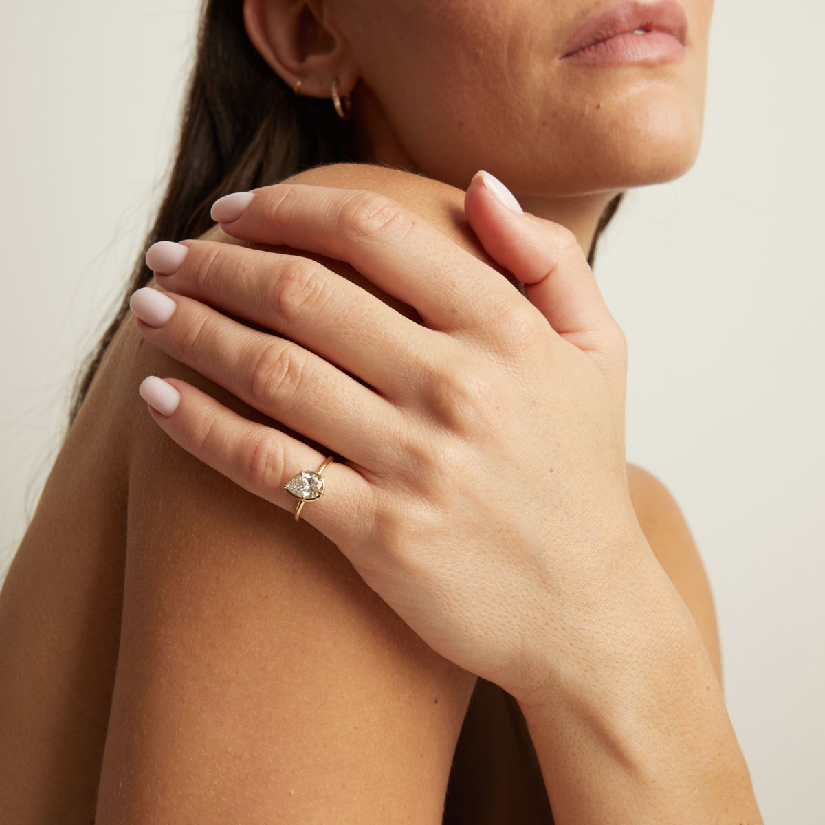 A close-up lifestyle shot of a woman wearing a delicate gold ring with a pear diamond. 