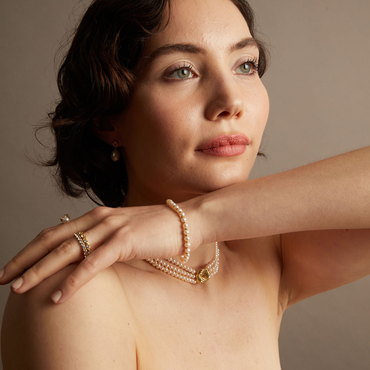Woman wearing various pearl jewelry on neutral background.