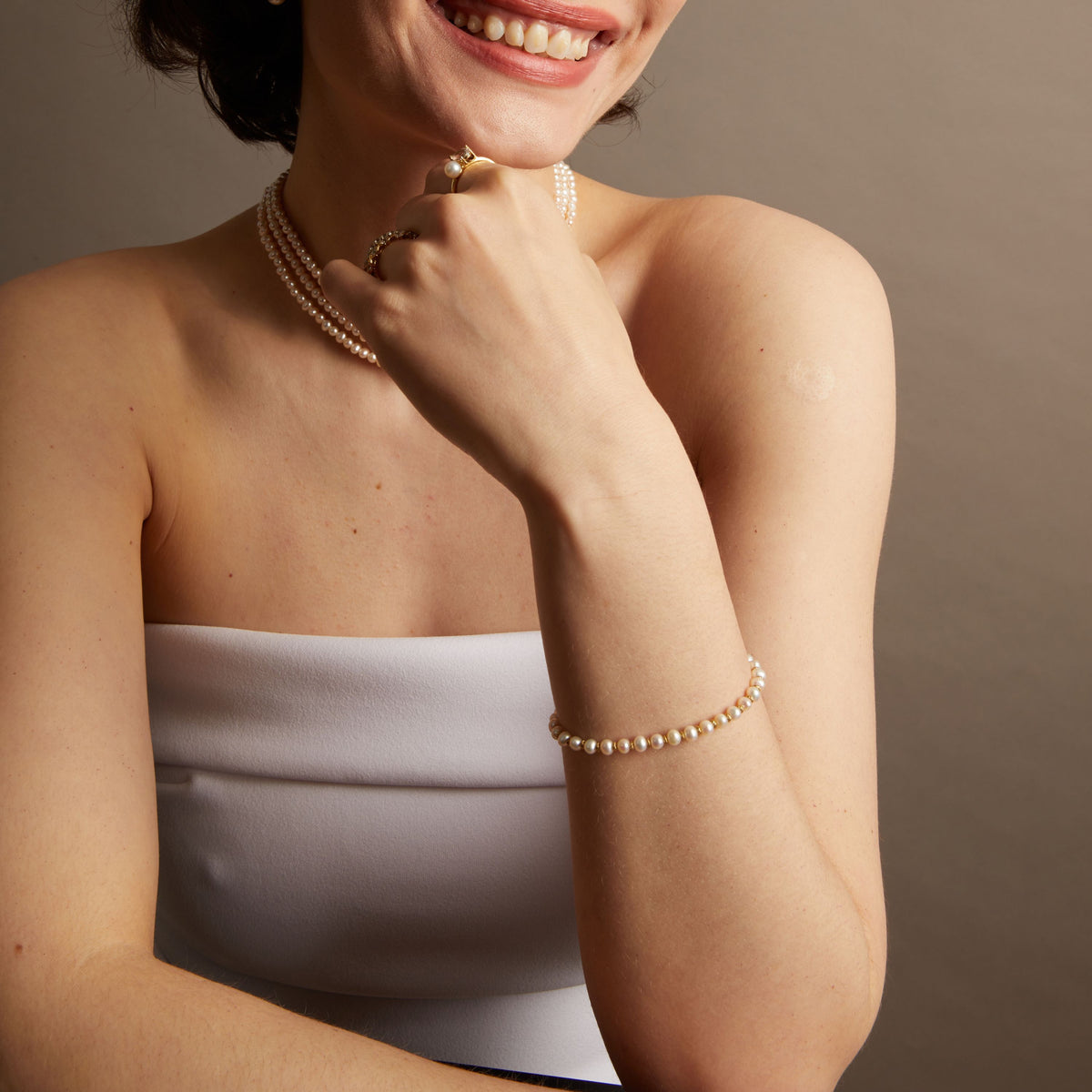 Woman wearing various pearl jewelry on neutral background.