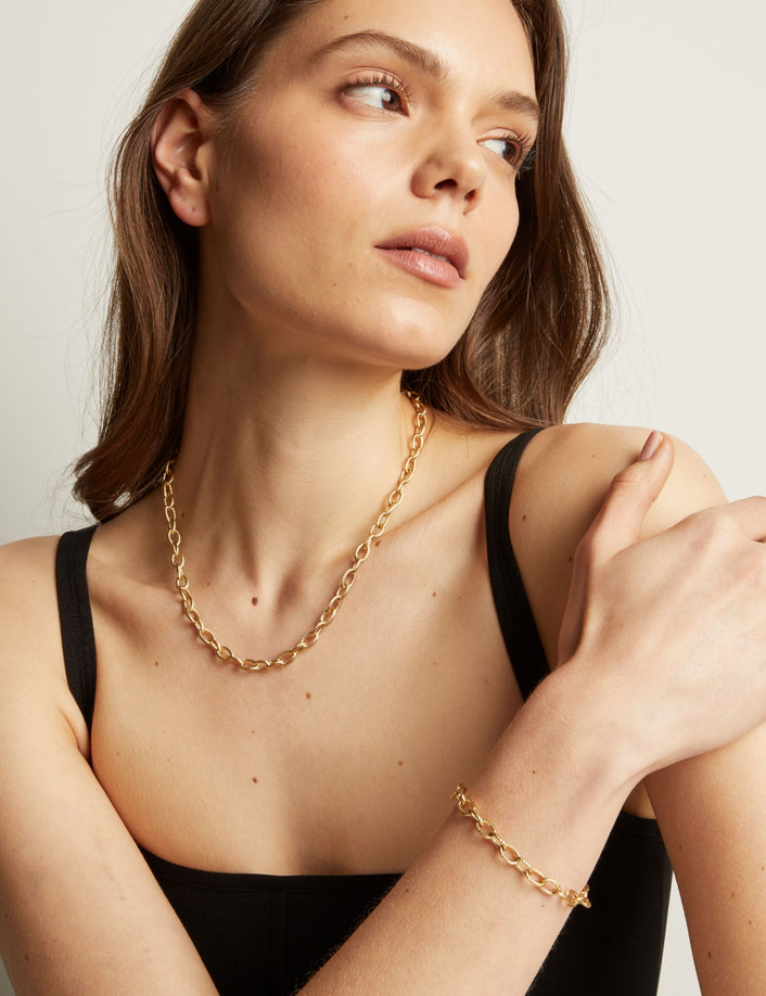 Model. Woman wearing a gold chain necklace and bracelet against a neutral background.