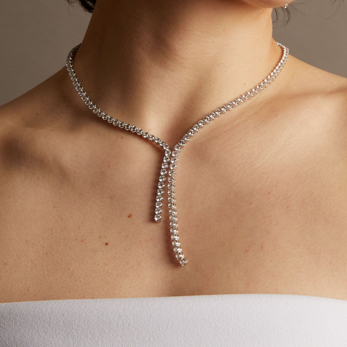 Close-up of a woman wearing a diamond necklace against a neutral background. 