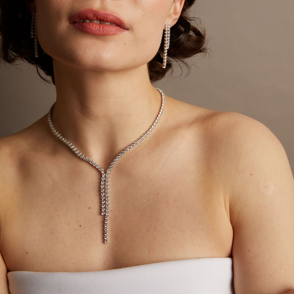 Close-up of a woman wearing a diamond necklace against a neutral background. 