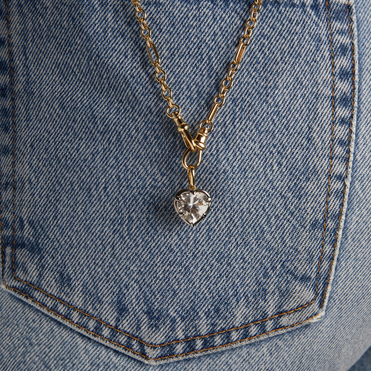Close up of a Heart Georgian Pendant on a chain resting on denim. 