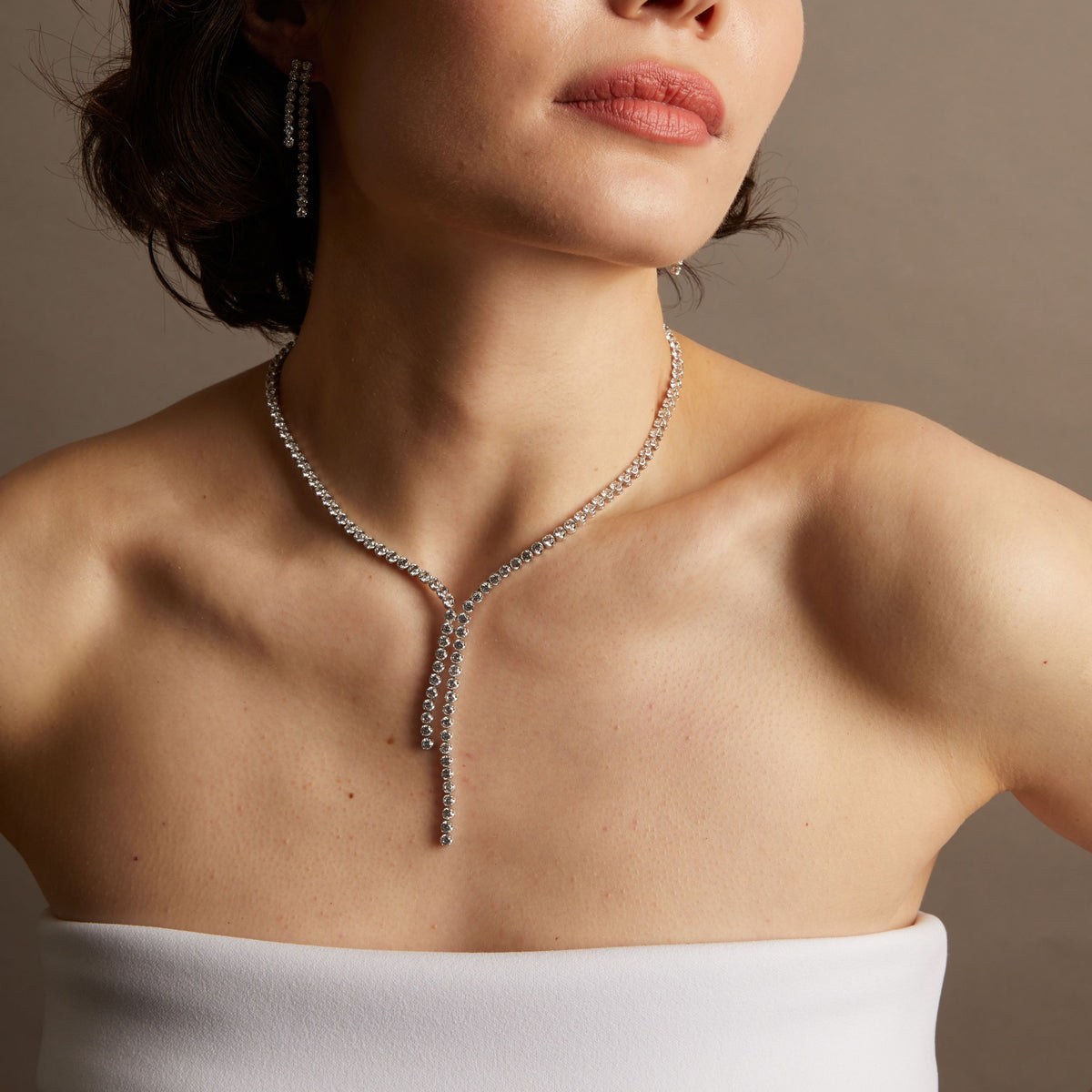 Close-up of a woman wearing a diamond necklace against a neutral background. 