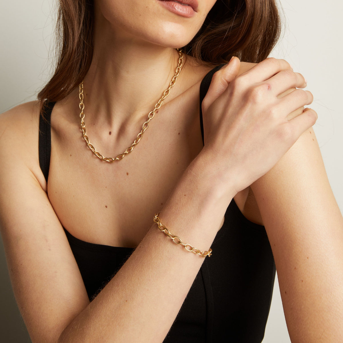Woman wearing a gold chain necklace and bracelet against a neutral background.