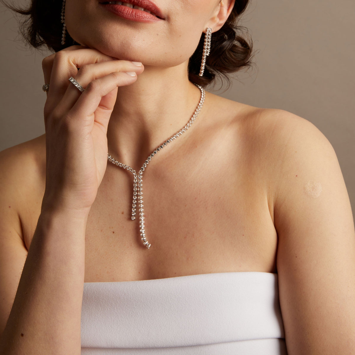 Close-up of a woman wearing a diamond necklace against a neutral background. 