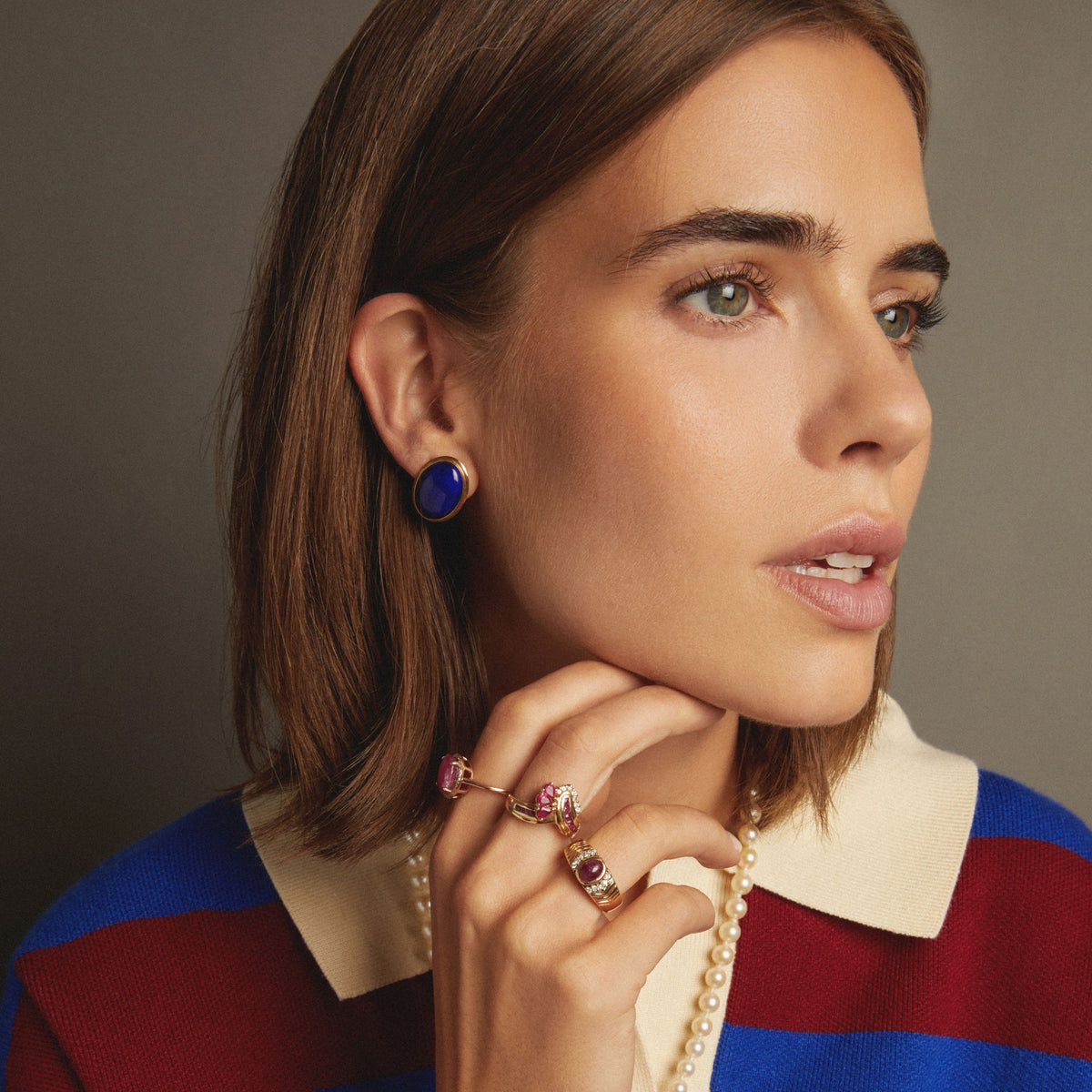 Model. Close up of woman wearing large blue stud earrings on neutral background