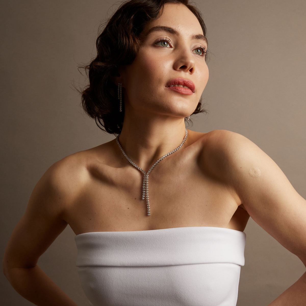 Close-up of a woman wearing a diamond necklace against a neutral background. 