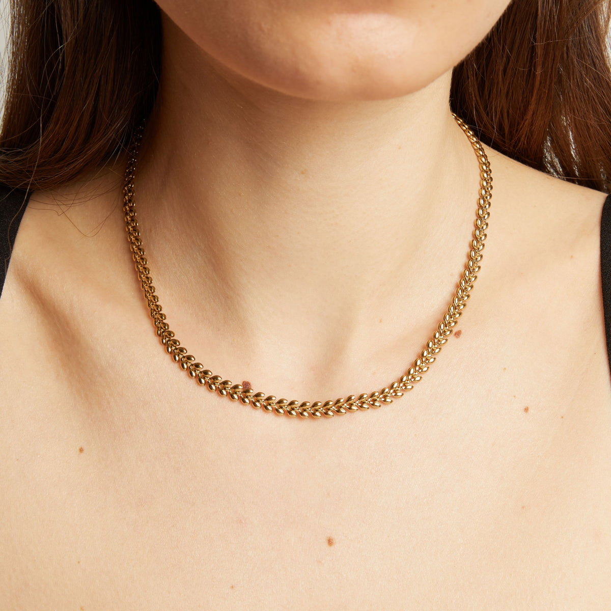 Model. Close up of a person wearing a gold chain necklace against a neutral background.