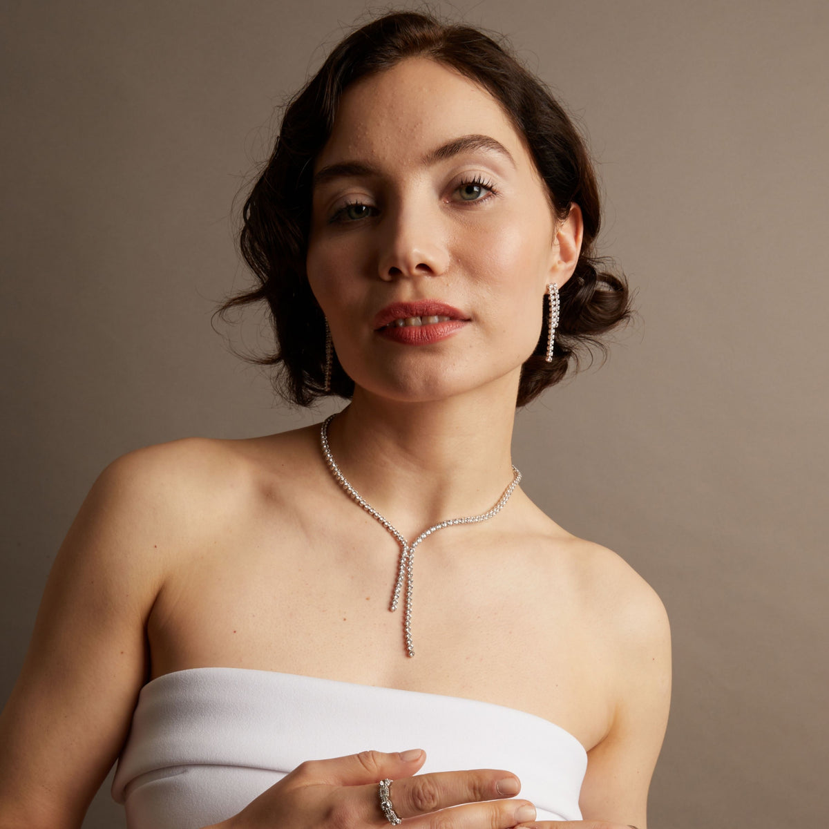 Close-up of a woman wearing a diamond necklace against a neutral background. 