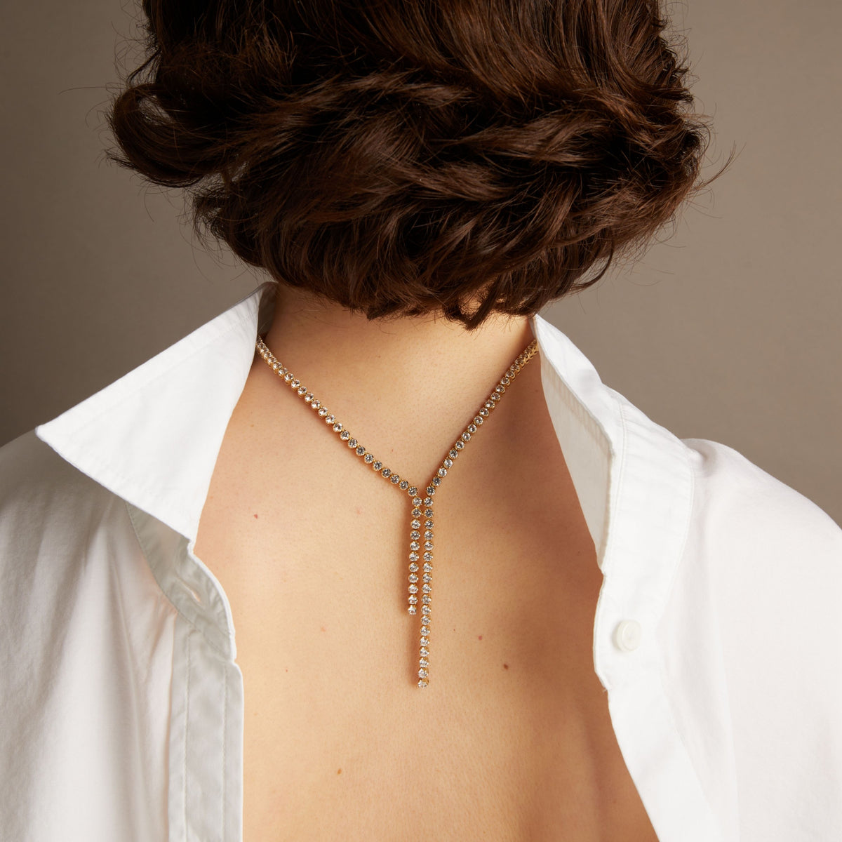 Close-up of a woman wearing a diamond necklace backwards on her back against a neutral background. 