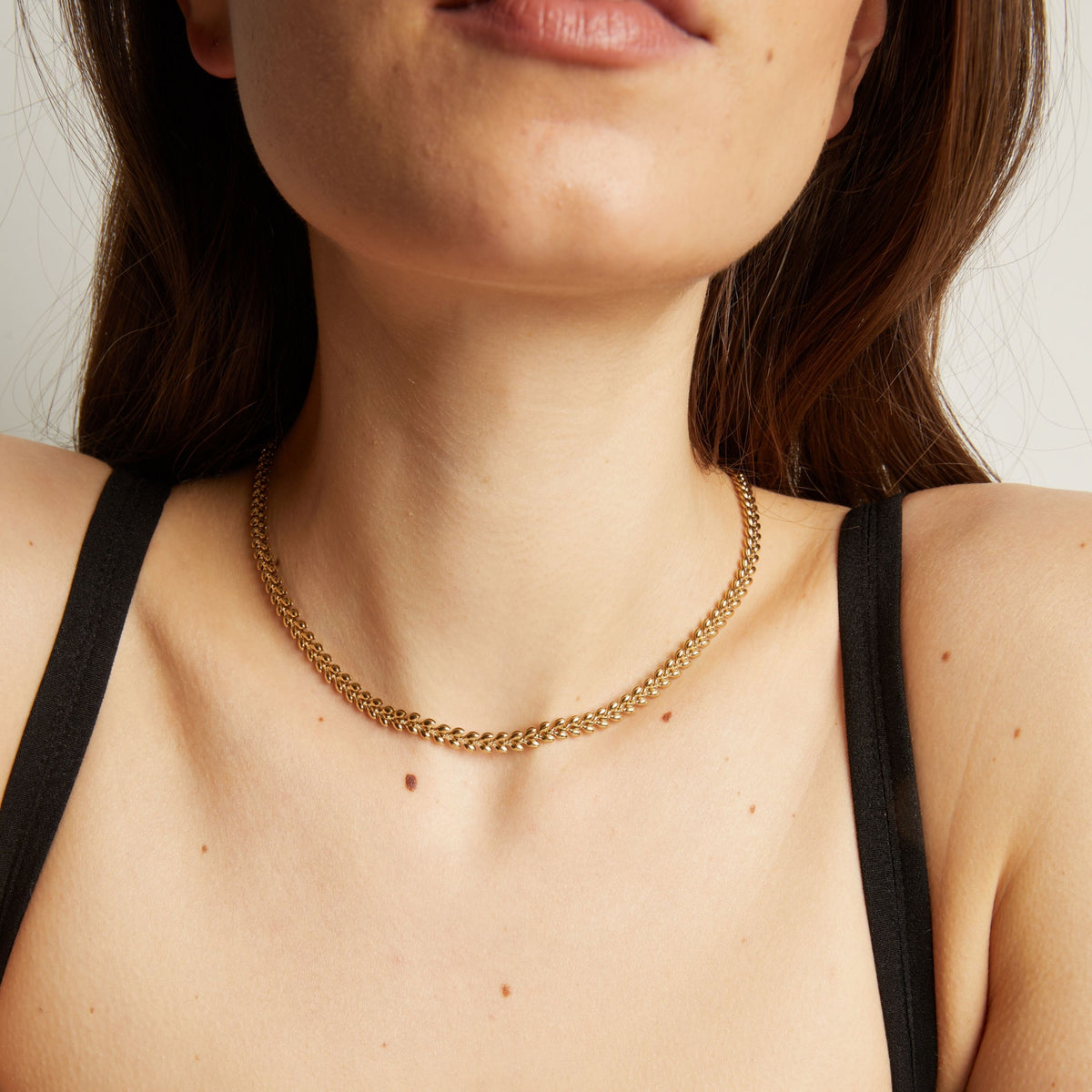 Close up of a person wearing a gold chain necklace against a neutral background.