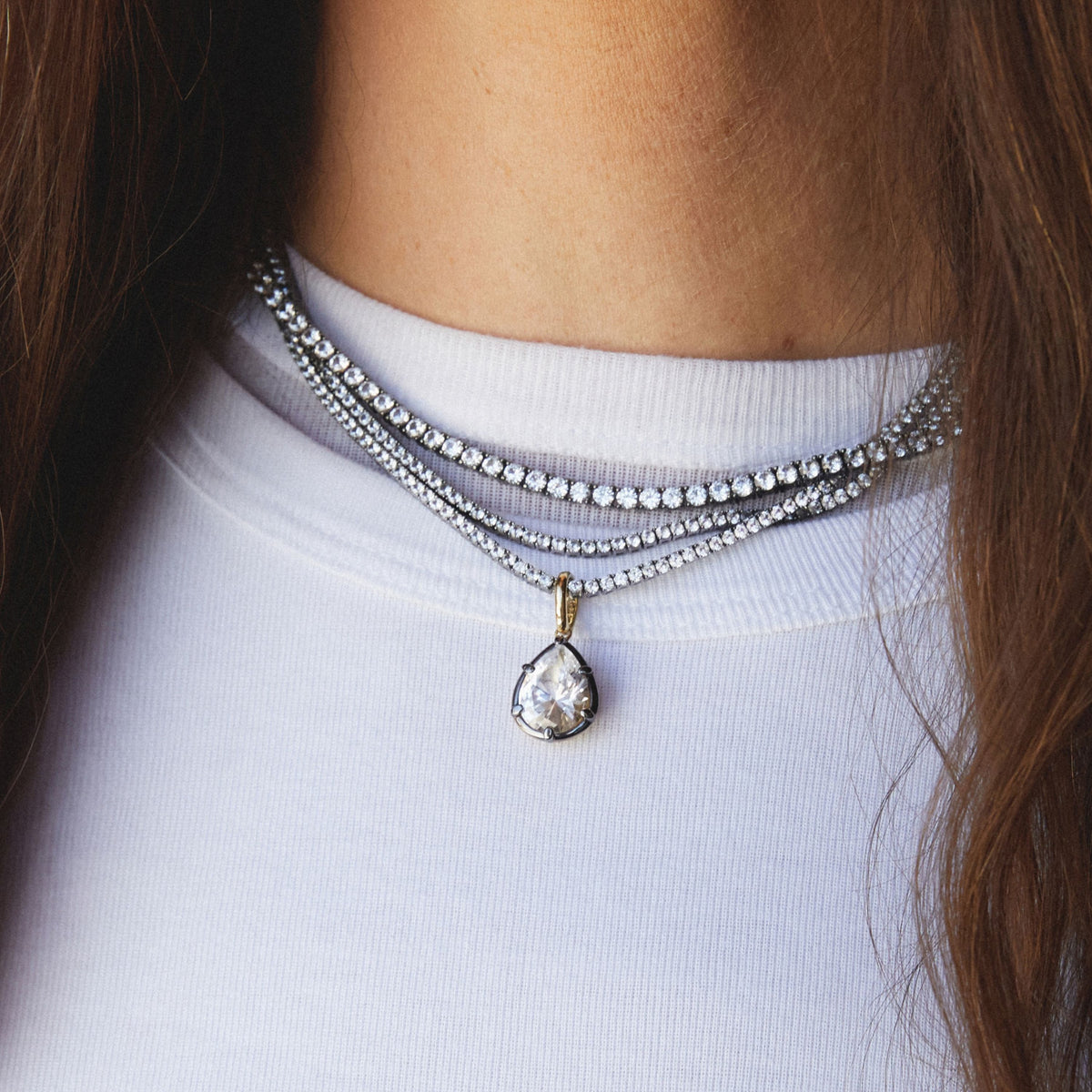 Model. Close up of woman wearing stacked tennis necklaces with a Pear Georgian Pendant. 