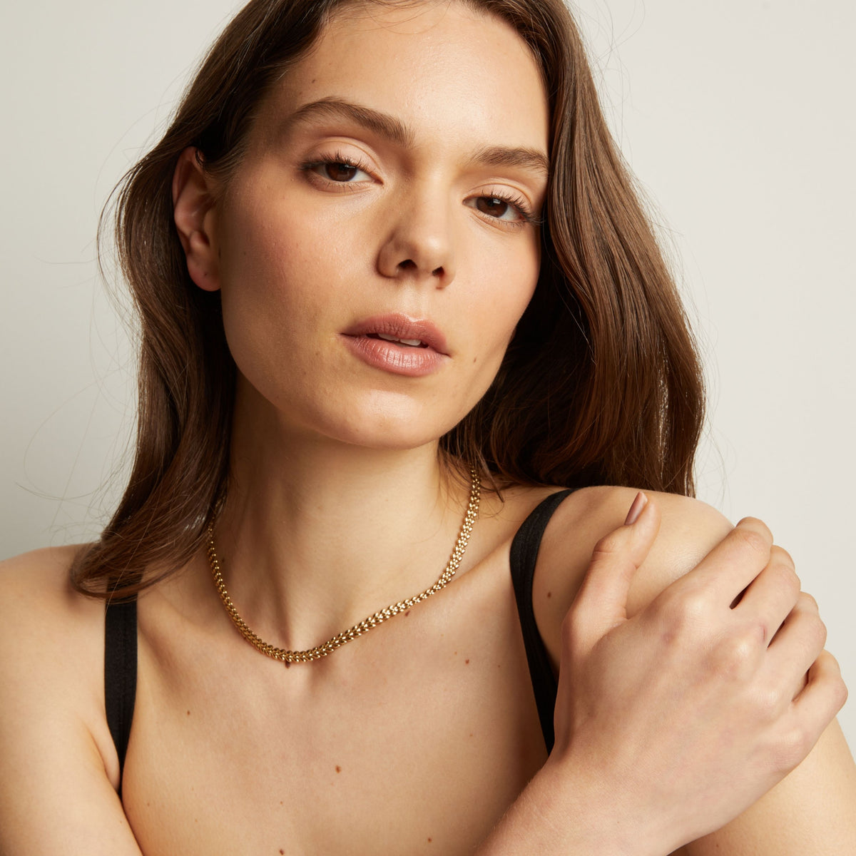 Model. Woman wearing gold necklace against a neutral background.