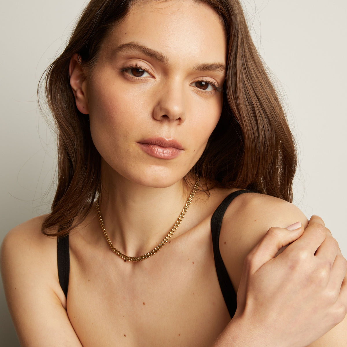 Model. Woman wearing gold necklace against a neutral background.