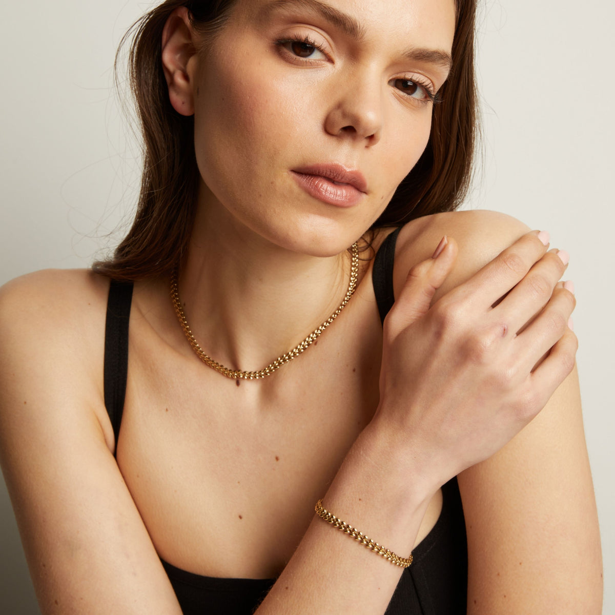 Model. Woman wearing gold necklace and bracelet against a neutral background.