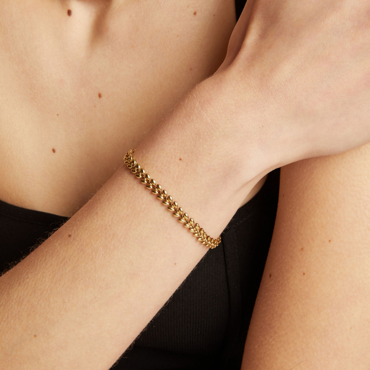 Model. Gold chain bracelet on a person's wrist with a neutral background.