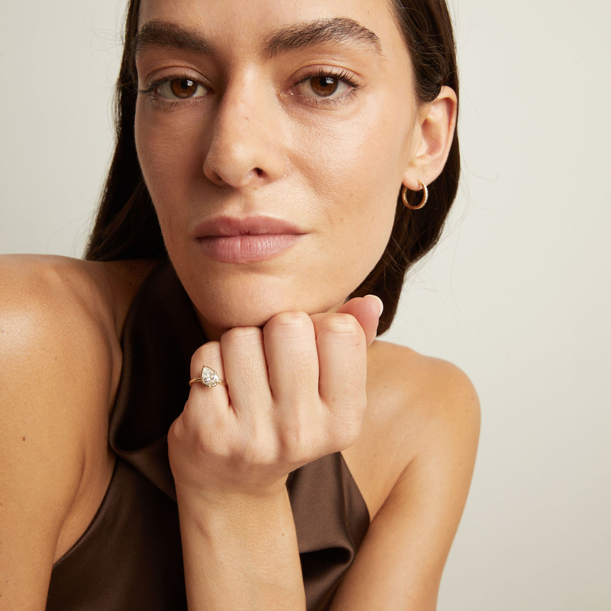 Model. A close-up lifestyle shot of a woman wearing a delicate gold ring with a pear diamond. 